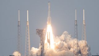 rocket launching with gray sky behind. two launch towers on either side surround the rocket