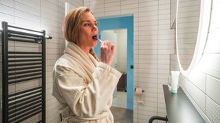 A woman with blonde hair brushes her teeth right before bed as part of her nighttime routine