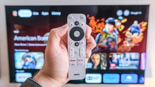 The onn 4K Google TV streaming box remote in front of a TV with the Google TV home screen