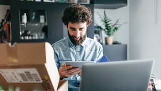 A man looking at a tablet with a brown Best Buy package on the desk in front of him