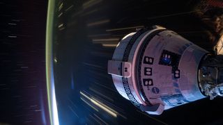 Long duration photograph of a space capsule in the lower right portion of the image and a blurred earth below with streaking lights. 