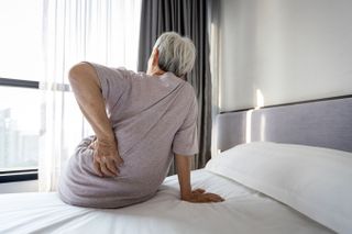 What types of mattresses are covered by Medicare, featuring an older woman holding her back whilst sitting on her bed