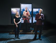 A stand with frames, with focus on the middle frame which shows a woman breastfeeding her baby. A man and a woman are standing in front of the art work