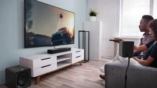 Klipsch Flexus soundbar, subwoofer and speaker in a modern living room with a big wall mounted TV and white media unit