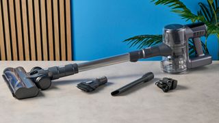 a closeup shot of the brush and crevice component tools of a modern-looking sleek shiny vacuum cleaner with light grey components on a carpet in front of a blue background