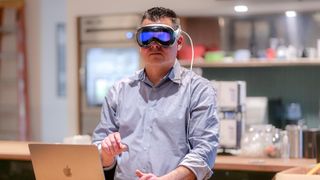 man wearing Apple Vision Pro headset in front of a MacBook