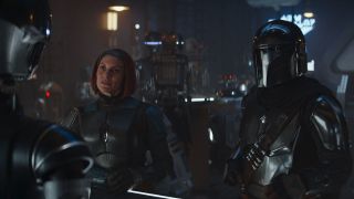 characters in futuristic silver armor talk to one another in a dingy bar