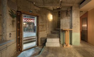 Glass door into bar showing the street outside, exposed concrete floor and walls and a simple wooden table