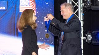 a smiling man gets set to drape a medal around a woman's neck
