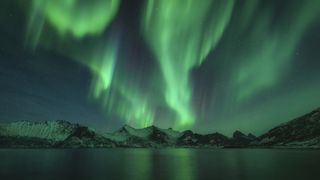 Mountains with background of northern lights and water below. 