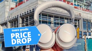 Bose QuietComfort Ultra Headphones being held up in front of urban building with price drop badge