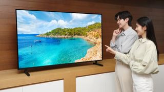 A prototype QD-OLED TV standing on a desk with two people pointing at the screen