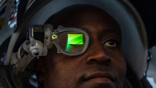 an astronaut wears a helmet that includes a glowing green screen in front of his right eye