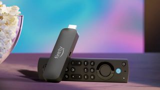 Amazon Fire TV Stick 4K Max (2023) propped up on its remote control in front of a TV and next to a bowl of popcorn