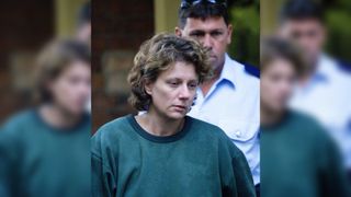 A woman in a green jumper with short brown hair being escorted out of a courtroom