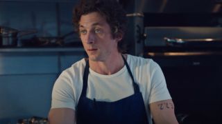 Jeremy Allen White as Carmy in The Bear wearing an apron and standing in a kitchen.