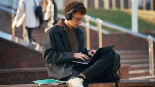 A student using a laptop near a college or university, sitting outside