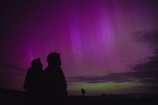 The silohettes of two people on a dazzling purple and green sky filled with auroras