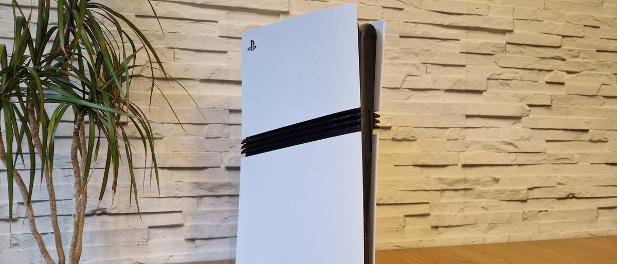 The PS5 Pro in front of a white brick background, next to a potted plant