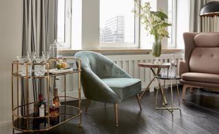 A sitting area with two armchairs, two round tables and a drinks trolley next to a window.