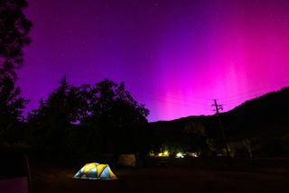 pink and purple northern lights over a tent that&#039;s lit from within in a campground