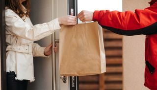 A deliveryman hands a bag to a woman waiting at her front door.