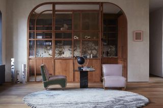 Bleecker Street by Tala Fustok Studio and Crina Architecture - a large circular grey rug on wood flooring, two old cushioned chairs, a side table with a globe.