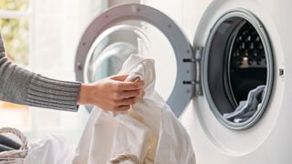 Woman loading washing machine with white sheet