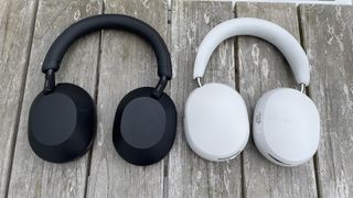 White Sonos Ace and black Sony WH-1000XM5 headphones lying side by side on a wooden table.