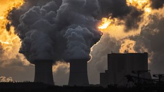 Smoke is pushed up from the towers of a power plant at sunset.