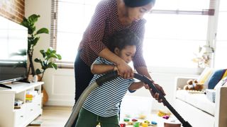 Woman hoovering room with young child