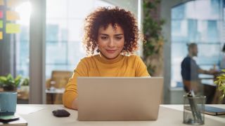 A woman sitting at at a table facing her laptop, smiling