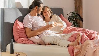 A couple lie on an Emma Original mattress while drinking tea