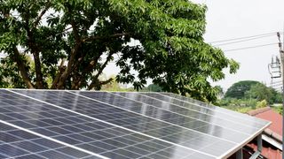 Solar panels on a roof with trees in the background casting a shadow