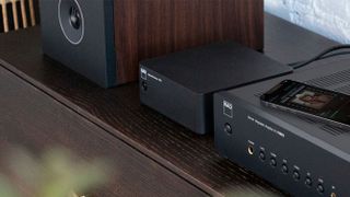 NAD CS1 music streamer on a hi-fi console with integrated amp and speakers