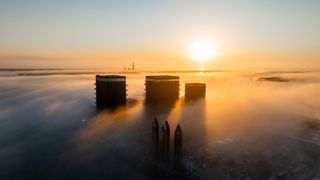 three rockets rise out of the fog with the sun low on the horizon