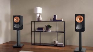A pair of black KEF Reference 1 Meta stand-mounted in front of a low shelving unit.