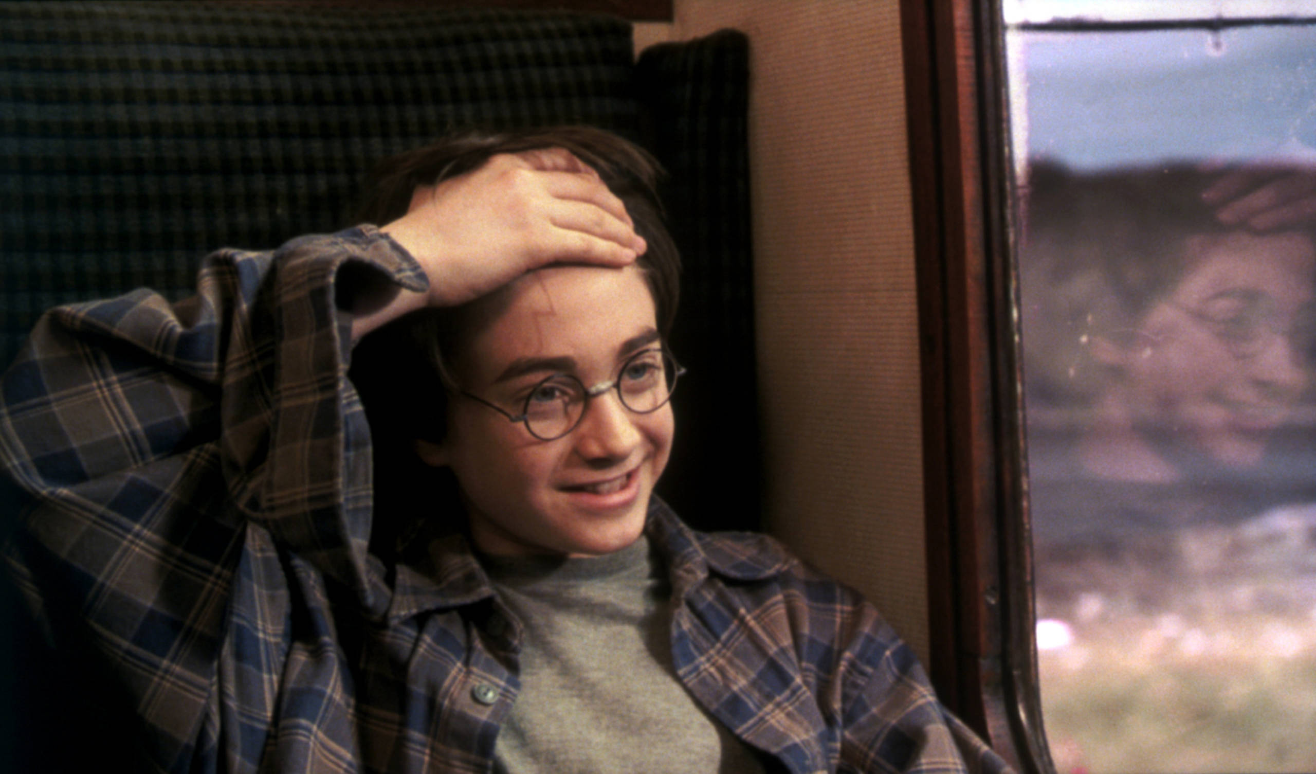 Harry Potter, sitting in a train car on the Hogwarts Express, lifts up his hair to reveal his lightning scar in Harry Potter and the Sorcerer’s Stone