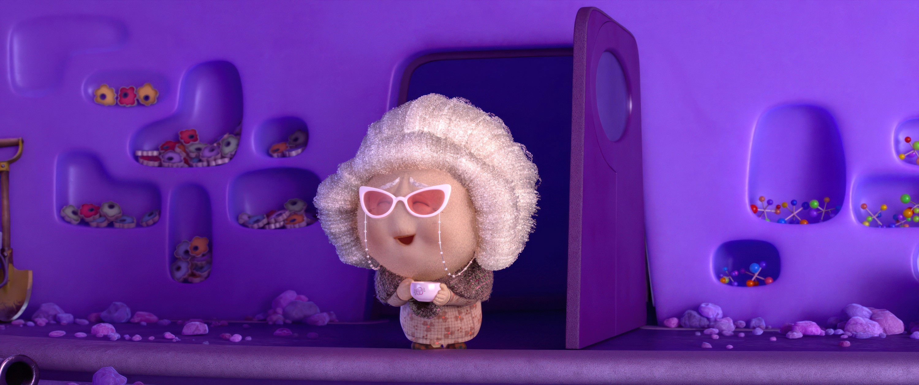 Nostalgia, a character from Pixar’s animated movie Inside Out 2, stands in a doorway. She looks like a little old lady with white hair, and pink cats-eye glasses attached to her face with a chain.