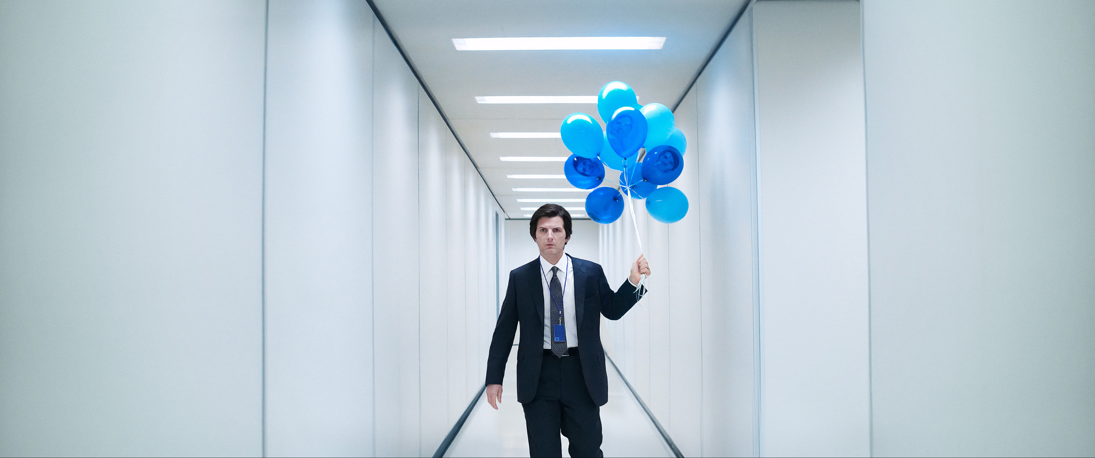 Mark (Adam Scott) standing in a hallway of Lumon Industries with balloons