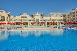 una grande piscina di fronte a un edificio con ombrelloni rossi di Bahia Principe Fantasia Tenerife - All Inclusive a San Miguel de Abona