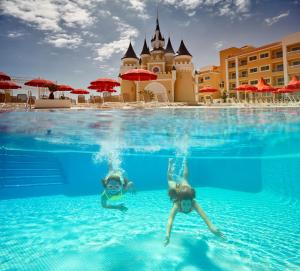 two people swimming in a pool in front of a hotel at Bahia Principe Fantasia Tenerife - All Inclusive in San Miguel de Abona