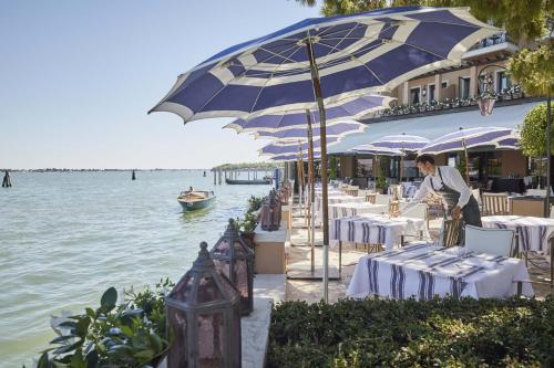 ein Restaurant mit Tischen und Sonnenschirmen neben dem Wasser in der Unterkunft Hotel Cipriani, A Belmond Hotel, Venice in Venedig