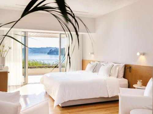 a bedroom with a white bed and a large window at Corfu Imperial, Grecotel Beach Luxe Resort in Kommeno