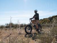 A man riding the RadExpand 5 Plus in Stone Tan on a rocky terrain. 