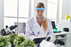 Young woman wearing scientist uniform writing on clipboard at laboratory