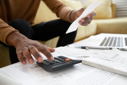 Close up of african American man calculating using machine managing household finances at home, focused biracial male make calculations on calculator paying bills, account taxes or expenses