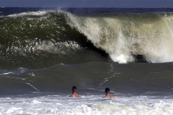 FILE - Shaun Clark, left, and Jim Donnelly watch as a big wave starts to come ashore at Fernandina Beach, in Nassau County, Fla., Sept. 16, 2003. A man on Florida’s east coast was bitten by a shark this weekend, but is now recovering, Nassau County authorities said Sunday, June 30, 2024, in the third shark attack in state waters over the past month. (Bob Mack/The Florida Times-Union via AP)