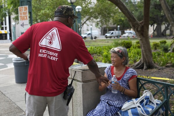 FILE - Ricky Leath, an outreach specialist with the City of Miami, talks with Bei Zhao, right, as he works with the Miami-Dade County Homeless Trust to distribute bottles of water and other supplies to the homeless population, helping them manage high temperatures, May 15, 2024, in Miami. The Miami-Dade government and the local National Weather Service office team up to treat heat like hurricanes and emphasize advanced preparations. (AP Photo/Lynne Sladky, File)
