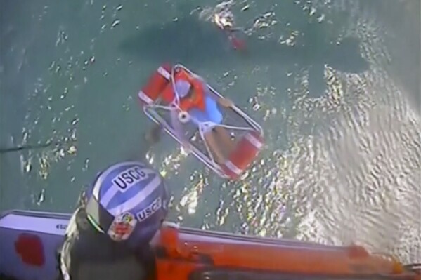 In this image taken from video provided by the U.S. Coast Guard a basket is lifted with person in it, Saturday, July 6, 2024. The helicopter from the Coast Guard air station in Detroit rescued five people who were clinging to a cooler in Lake Erie waters about 10 miles (16 kilometers) off Ashtabula, Ohio after their 22-foot boat had been swamped by a wave, officials said. (U.S. Coast Guard via AP)